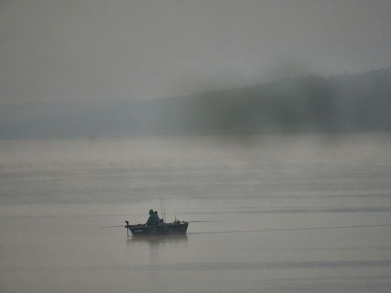 Pescador posicionando-se na margem de um lago cercado de árvores